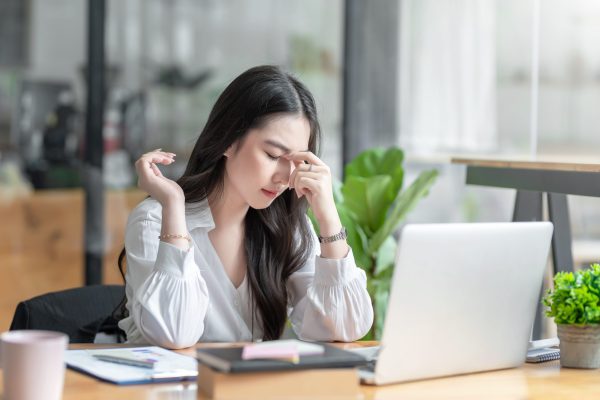 Young Asian woman feeling migraine head strain. Tired, Overworked businesswoman financier while working on laptop computer in office.